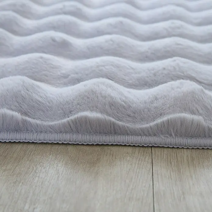 Fellteppich Ambiance - Silber, 250 x 80 cm, 100 % Polyester - Nahaufnahme eines grauen, gewellten Teppichs mit weicher Textur, der auf einem Holzboden liegt. Ideal für Wohnzimmer und Schlafzimmer.