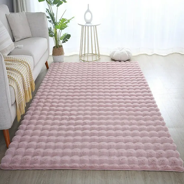 Fellteppich Ambiance - Rosa, 170 x 120 cm, 100 % Polyester - Nahaufnahme eines rosa, hochflorigen Teppichs mit Noppenstruktur in einem hellen Wohnzimmer mit Sofa und Beistelltisch.