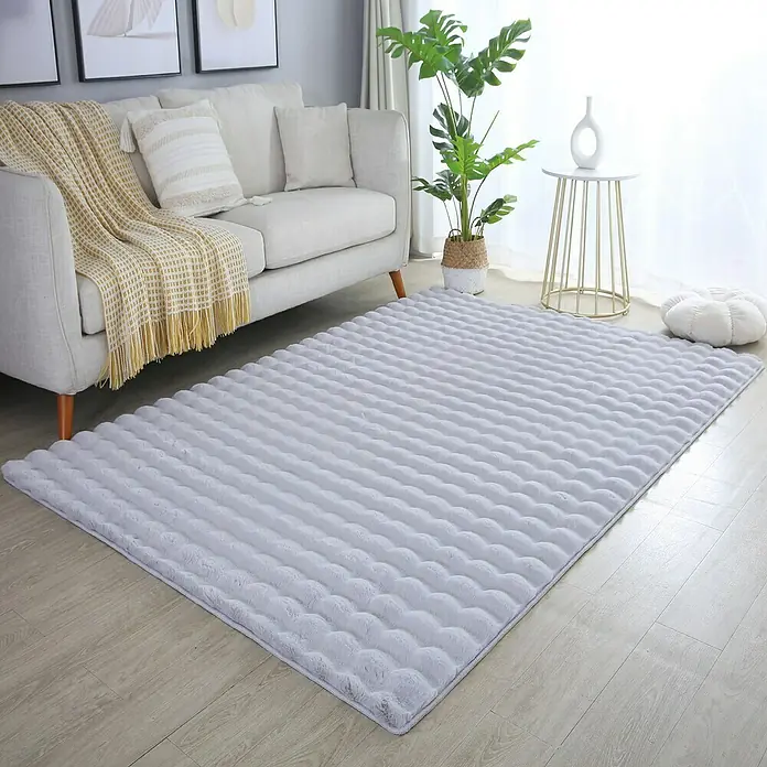 Fellteppich Ambiance - Silber, 250 x 80 cm, 100 % Polyester - Ein weicher, grauer Teppich mit gerippter Textur liegt in einem hellen Wohnzimmer mit Sofa und Pflanzen.
