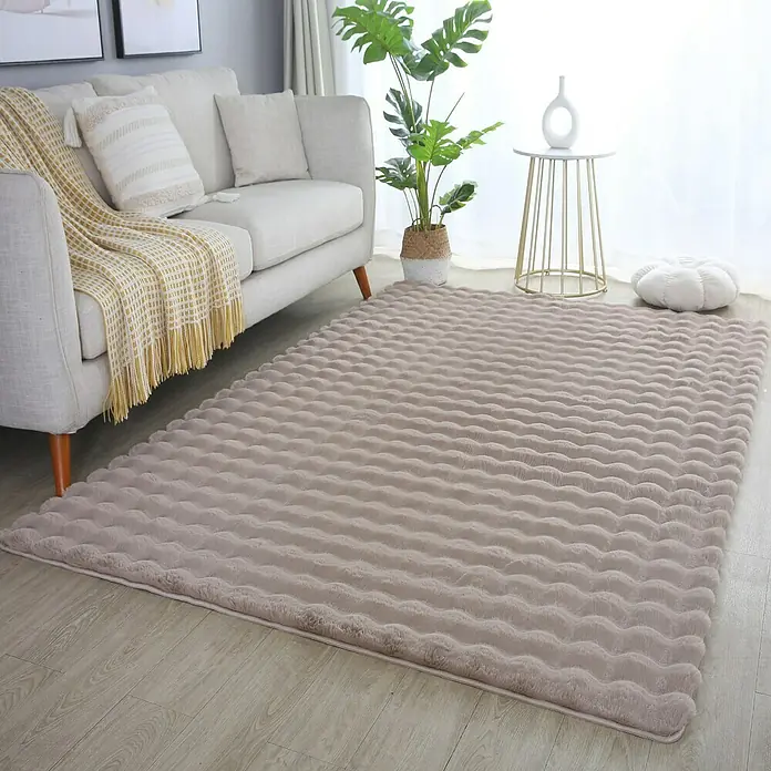 Fellteppich Ambiance - Beige, 200 x 140 cm, 100 % Polyester - Ein weicher, beiger Teppich mit wellenförmiger Textur liegt in einem gemütlichen Wohnzimmer.