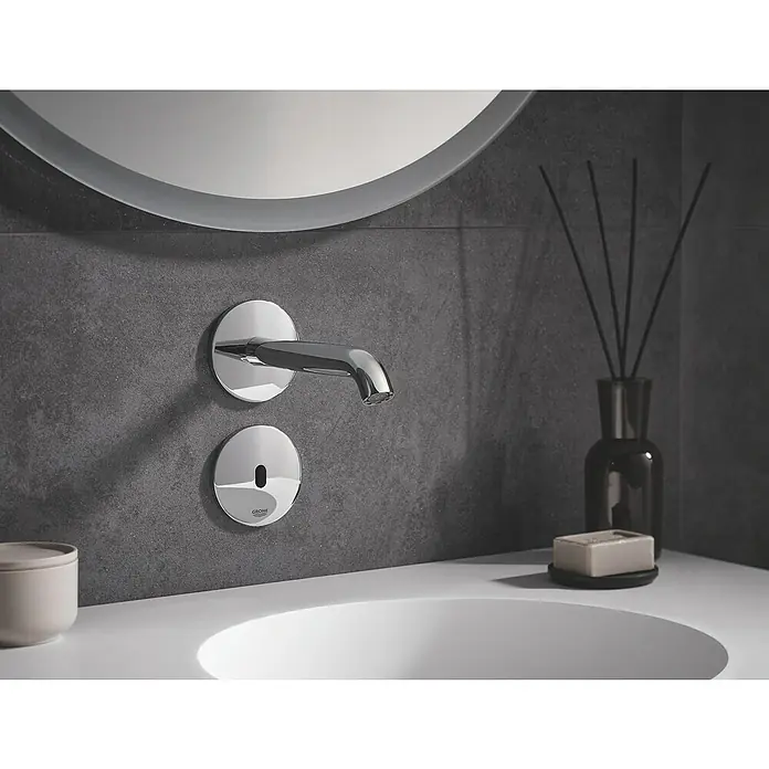 Grohe Essence Waschtischarmatur E - Wandmontage, Chrom, Glänzend, Ausladung Armatur: 182 mm - Nahaufnahme eines stilvollen, berührungslosen Grohe Waschtischarmatur mit einer schlanken, runden Spiegeloberfläche und modernen Duftstäbchen.