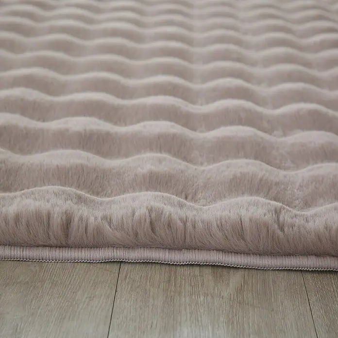 Fellteppich Ambiance - Beige, 200 x 140 cm, 100 % Polyester - Nahaufnahme eines lavendelfarbenen Teppichs mit gewellten Texturen, der auf einem hellen Holzboden liegt.
