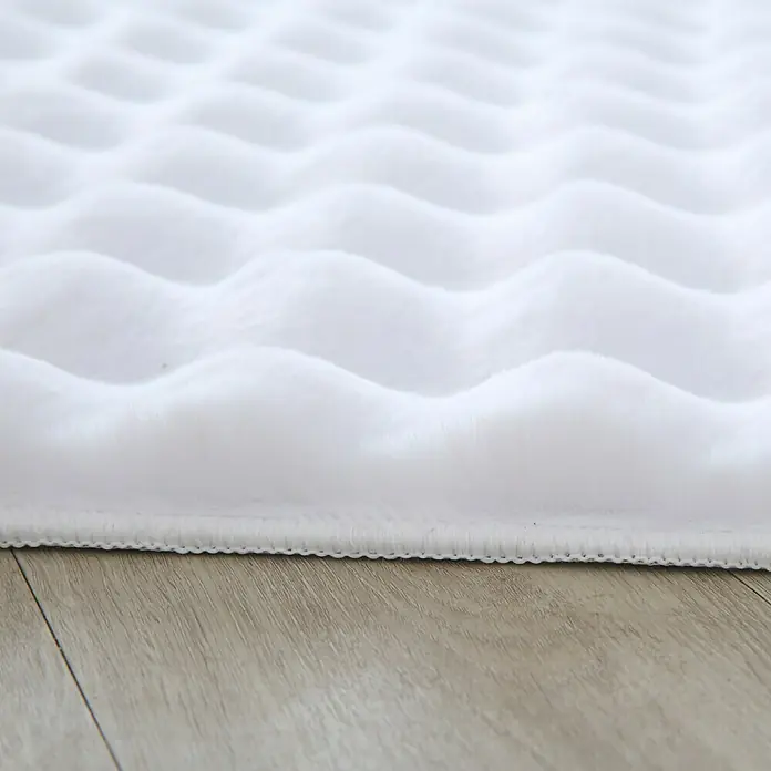Fellteppich Ambiance - Weiß, 250 x 80 cm, 100 % Polyester - Nahaufnahme eines weichen, weißen Teppichs mit Wellenmuster, der auf einem hellen Holzboden liegt.