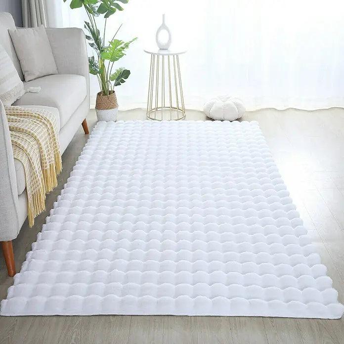 Fellteppich Ambiance - Weiß, 250 x 80 cm, 100 % Polyester - Ein weicher, weißer Teppich mit Noppen liegt in einem hellen Wohnzimmer, neben einem Sofa und einem Beistelltisch.