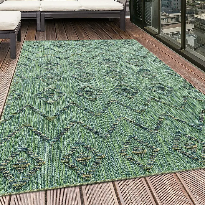 Outdoor-Teppich Bahama IV - Grün, 250 x 80 cm, 100 % Polypropylen - Ein grüner Outdoor-Teppich mit geometrischen Mustern liegt auf einer Holzterrasse neben Terrassenmöbeln und einer Glaswand.