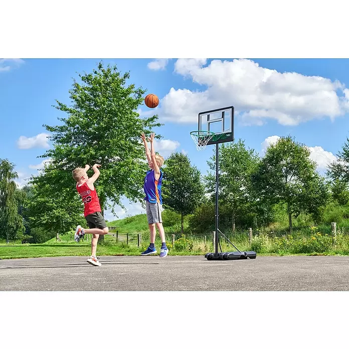 Salta Basketballkorb Dribble - Schwarz - Zwei Jungen spielen Basketball mit einem mobilen Korb mit schwarzem Ständer, transparenter Platte und grünem Ring im Freien.