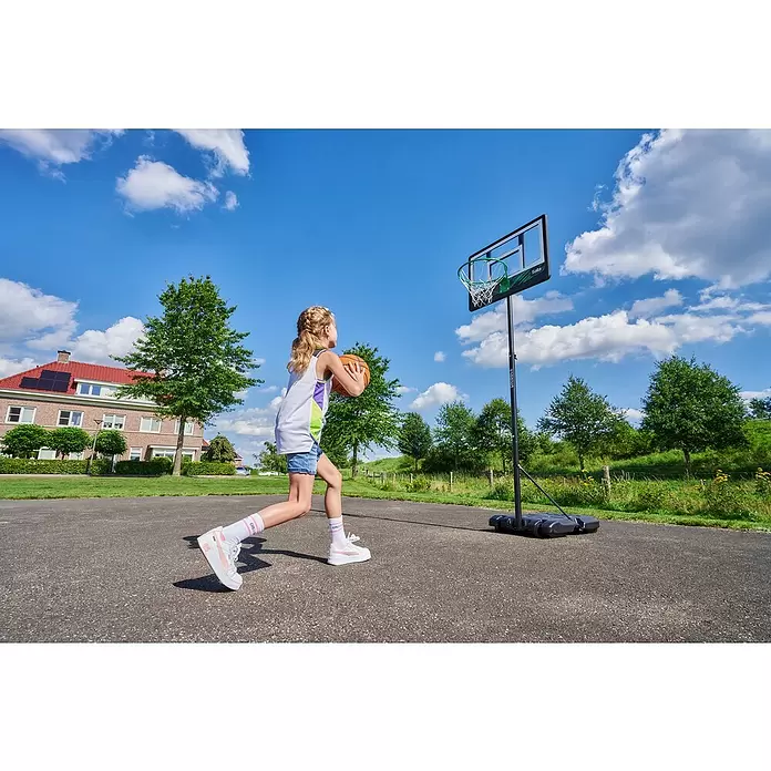 Salta Basketballkorb Dribble - Schwarz - Ein Mädchen dribbelt einen Basketball auf einen tragbaren, schwarz gerahmten Korb mit grünem Ring im Freien.