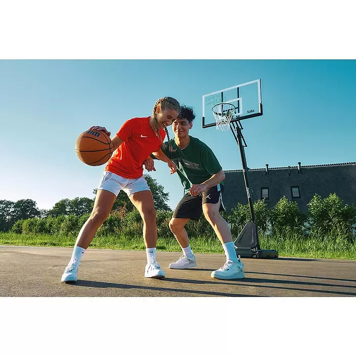 Salta Basketballkorb Guard - Schwarz, Höhe: 371 cm - Zwei junge Erwachsene spielen Basketball im Freien mit einem tragbaren Korb und dribbeln einen Ball.