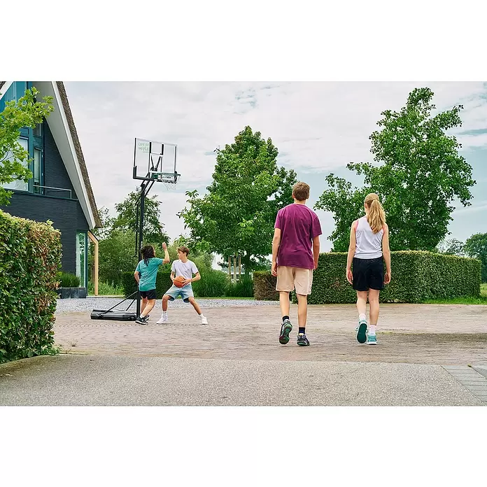 Salta Basketballkorb Center - 234 x 210 x 125 cm, Schwarz - Kinder spielen Basketball mit einem tragbaren Korb auf einer gepflasterten Einfahrt vor einem Haus.