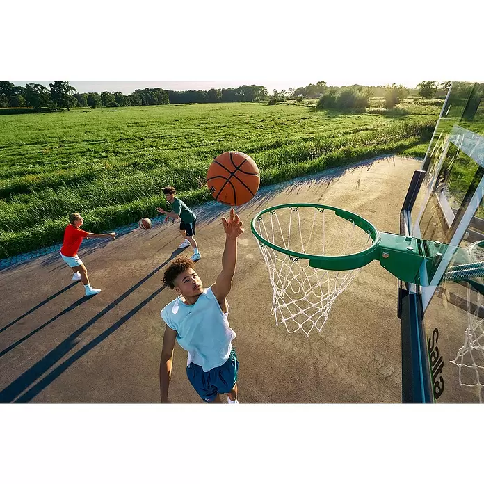 Salta Basketballkorb Guard - Schwarz, Höhe: 371 cm - Eine Person spielt Basketball, im Begriff in einen grünen Outdoor-Korb mit weißem Netz zu dunken.