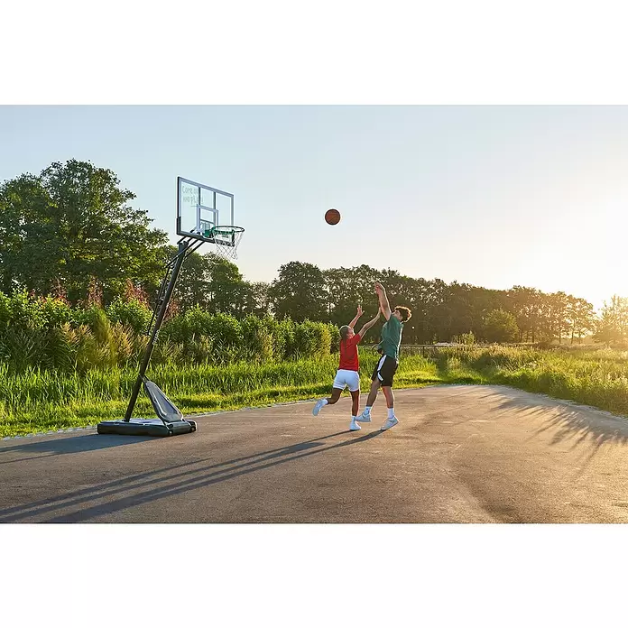 Salta Basketballkorb Guard - Schwarz, Höhe: 371 cm - Zwei Personen spielen draußen Basketball mit einem tragbaren Korb mit transparenter Platte und grünem Ring.
