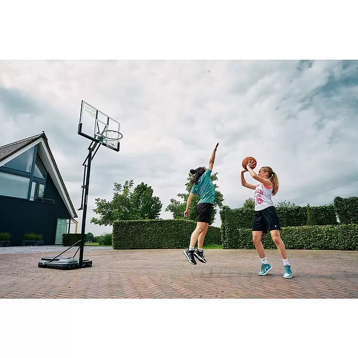 Salta Basketballkorb Center - 234 x 210 x 125 cm, Schwarz - Tragbarer Basketballkorb mit transparenter Platte und grünem Ring, von zwei Kindern im Freien genutzt.