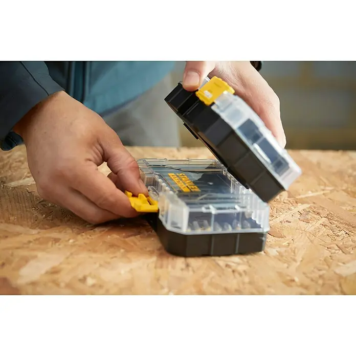 Stanley FatMax Set de puntas STA88557-XJ - 32 pzs. - Una persona cerrando un organizador negro Stanley Fatmax con cierres amarillos sobre una superficie de madera.