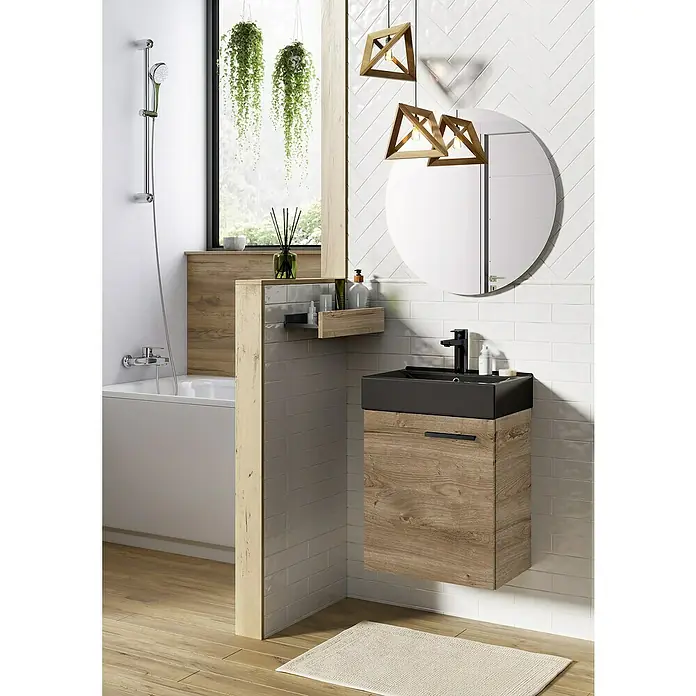 Badmöbel-Set Tiny - Gesamtbreite Badmöbel: 45 cm, Eiche/Schwarz, Matt, DIN Anschlag: Links/Rechts, 2 -tlg. - Badezimmer-Interieur mit einem modernen Waschtischunterschrank in Holzoptik, einem runden Spiegel und hängenden Pflanzen am Fenster.