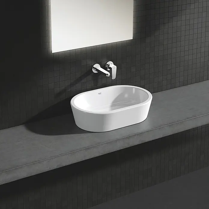 Grohe Eurodisc Cosmopolitan Waschtischarmatur - Wandmontage, Chrom, Glänzend, Ausladung Armatur: 170 mm - Nahaufnahme eines modernen, weißen Aufsatzwaschbeckens von Grohe, montiert auf einer grauen Arbeitsplatte vor einer dunklen Mosaikwand.