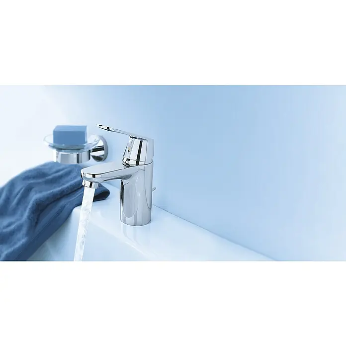 Grohe Eurosmart Cosmopolitan Waschtischarmatur S-Size - Ohne Zugstange, Chrom, Glänzend - Nahaufnahme eines modernen Chrom-Wasserhahns mit fließendem Wasser in einem sauberen Waschbecken, daneben Seife und ein Tuch.