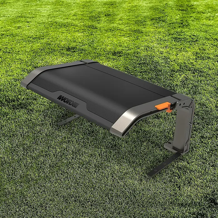 Worx Landroid Mähroboter-Garage - L x B x H: 706,3 x 554 x 397,5 mm, Schwarz, Worx Landroid Mähroboter - Detailaufnahme eines WORX-Gartengeräts auf Rasen. Das Gerät hat eine schwarze Oberfläche mit grauen Akzenten und einem orangefarbenen Knopf.