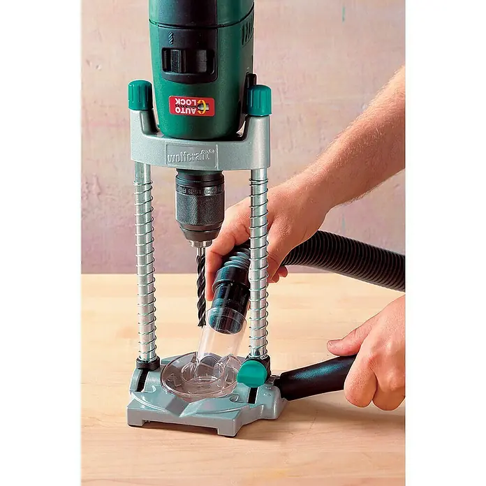 Wolfcraft Bohrständer Tec-Mobil - Schwenkbar bis ± 45° - Das Bild zeigt eine Bohrmaschine mit Bohrständer und Absaugvorrichtung auf einem Holztisch. Die Bohrmaschine ist grün und grau.