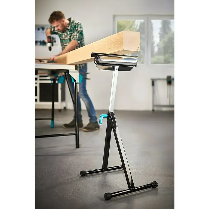 Wolfcraft Multifunktions-Auflagebock - Arbeitshöhe: 630 mm - 1.000 mm, Belastbarkeit: 50 kg - Das Bild zeigt einen Rollbock für die Holzbearbeitung, der die Handhabung langer Werkstücke erleichtert, während ein Mann im Hintergrund arbeitet.