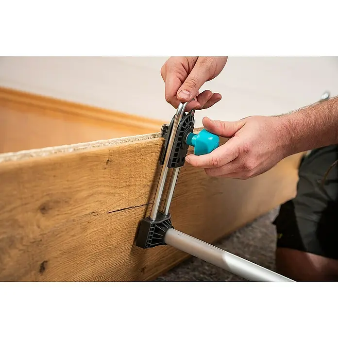 Wolfcraft Türfuttermontagestrebe Easy - Passend für: Türen mit 600 - 1.000 mm Breite - Ein Wolfcraft-Produkt wird verwendet, um ein Holzbrett zu befestigen. Der Mann dreht einen blauen Knopf, um das Werkzeug anzupassen.