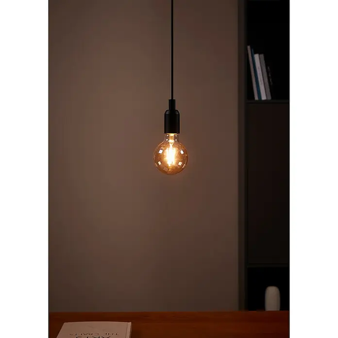 Eglo Bombilla LED Ámbar - E27, No regulable, Blanco cálido, 330 lm, 4 W, G95 - Primer plano de una bombilla Edison con un accesorio negro, suspendida del techo, que emite un brillo cálido. Una iluminación atmosférica.