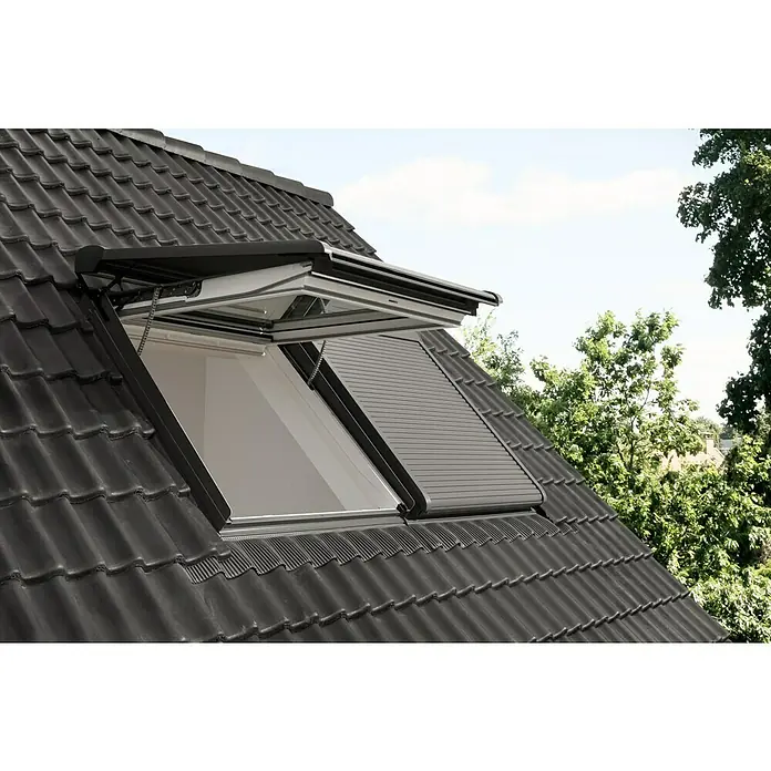Velux Active Sensor Raumklima KLA 300 - Passend für: VELUX ACTIVE Starter-Set with NETATMO KIX 300 - Nahaufnahme eines Dachfensters mit Rollladen, das in ein Ziegeldach eingebaut ist und einen Blick auf den Himmel und grüne Bäume bietet.