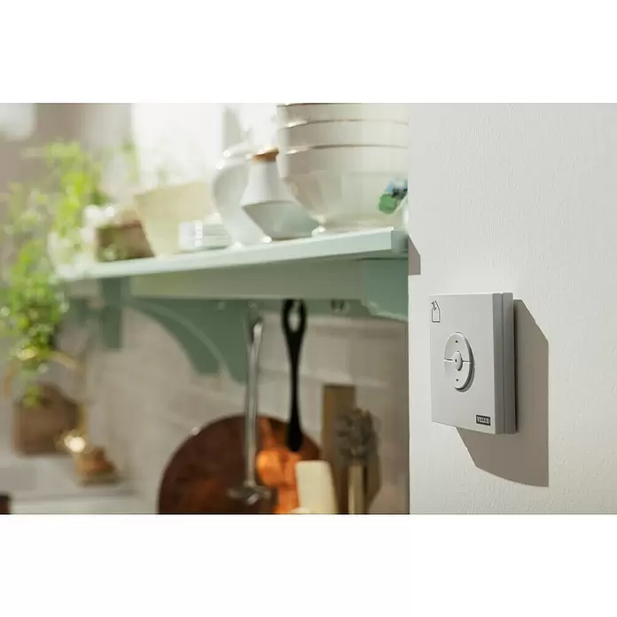Velux Funk-Wandschalter Fenster KLI 311 - Passend für: VELUX Fenstermotoren (io-homecontrol®) - Hellgraues, wandmontiertes Smart-Bedienfeld mit Richtungstasten und Fenstersymbol in häuslicher Umgebung.