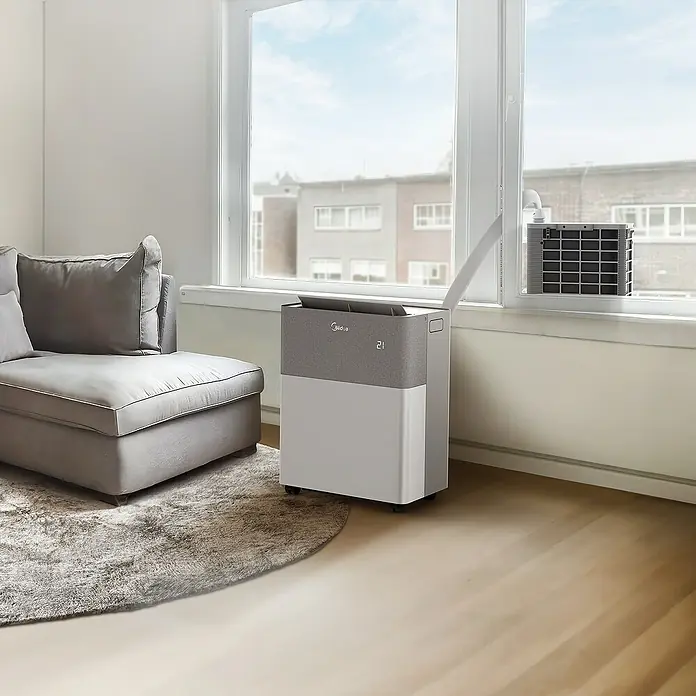 Midea Klimasplitgerät PortaSplit 12.000 Btu - Kühlleistung: 3.500 W, Heizleistung: 3.500 W, Raumgröße: 42 m² - Ein tragbares Klimagerät von Midea steht in einem Wohnzimmer neben einem Sofa und kühlt den Raum effektiv.