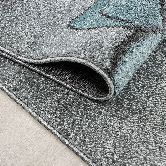 Kinderteppich Kids 0580 - Blau, 200 x 140 cm, 100 % Polypropylen - Detailansicht eines grauen Teppichs mit modernem Muster, aufgerollt, um die Textur und Verarbeitung zu zeigen.