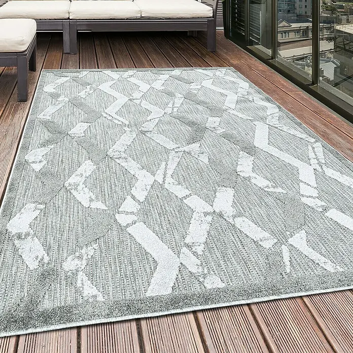 Outdoor-Teppich Bahama VII - Grau, 200 x 140 cm, 100 % Polypropylen - Ein grauer Outdoor-Teppich mit abstraktem Muster liegt auf einer Holzterrasse neben Gartenmöbeln.
