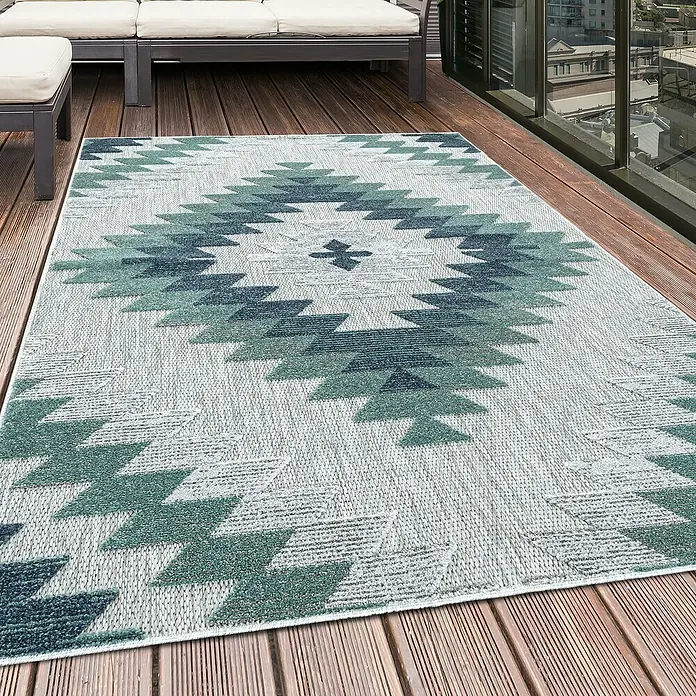 Outdoor-Teppich Bahama II - Blau, 200 x 140 cm, 100 % Polypropylen - Ein grauer Outdoor-Teppich mit einem blaugrünen geometrischen Muster liegt auf einer Holzterrasse und sorgt für einen stilvollen Look.