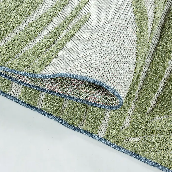 Outdoor-Teppich Bahama VIII - Grün, 250 x 80 cm, 100 % Polypropylen - Detailaufnahme eines grünen Teppichs mit geometrischem Muster und blauer Bordüre, teilweise aufgerollt, um die Unterseite zu zeigen.