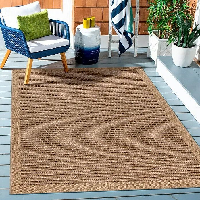 Outdoor-Teppich Dhaka II - Schwarz, 200 x 140 cm, 100 % Polypropylen - Ein rechteckiger, brauner Outdoor-Teppich liegt auf einer blauen Holzterrasse und schafft eine gemütliche Atmosphäre im Außenbereich.