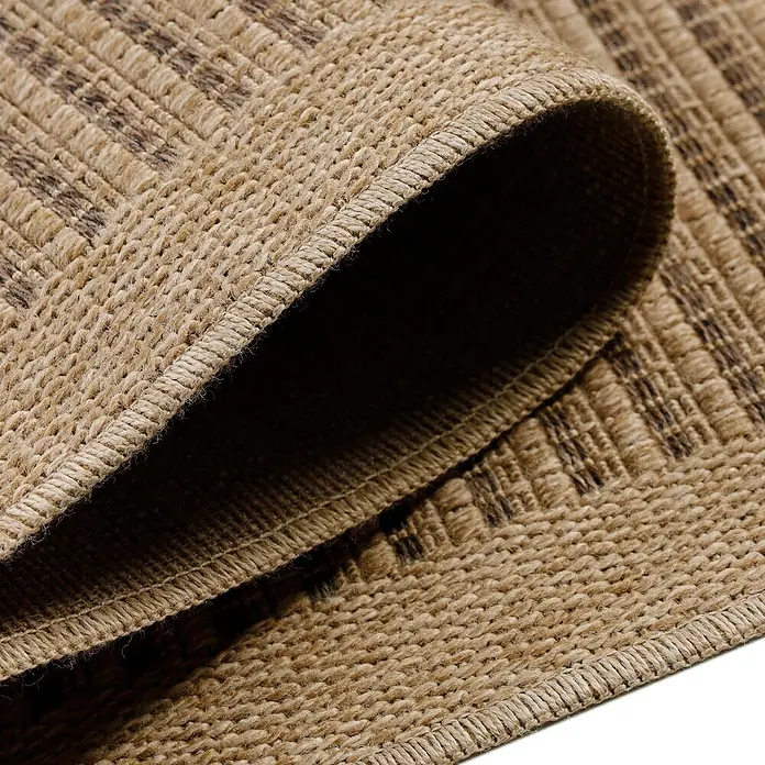 Outdoor-Teppich Dhaka II - Schwarz, 200 x 140 cm, 100 % Polypropylen - Nahaufnahme eines gewebten Teppichs mit braunen Akzenten und gerollter Kante, die die Textur und Verarbeitung hervorhebt.