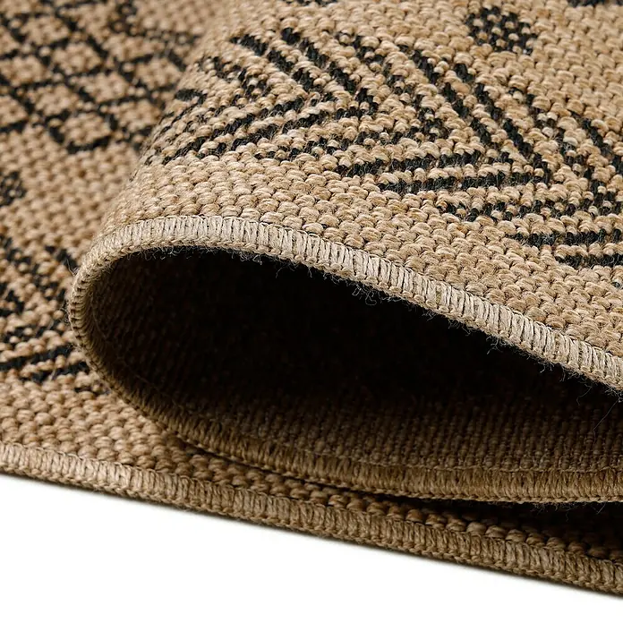 Outdoor-Teppich Dhaka I - Schwarz, 200 x 140 cm, 100 % Polypropylen - Detailaufnahme eines gerollten Teppichs mit geometrischem Muster in Beige und Schwarz, das die Textur und Verarbeitung hervorhebt.