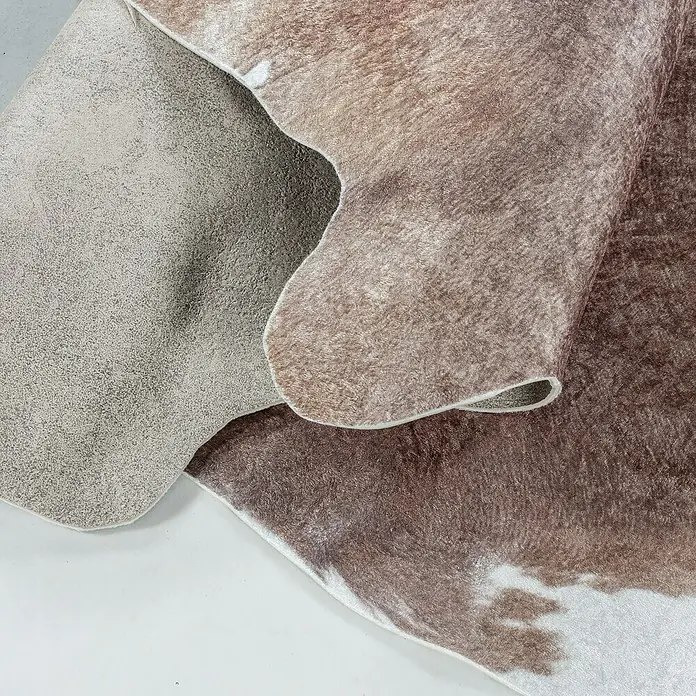 Flachgewebeteppich Etosha - Kuh, Braun, 200 x 150 cm, 100 % Polyester - Nahaufnahme einer kunstvollen Kuhfellimitat-Decke, die Textur und Muster detailreich hervorhebt.