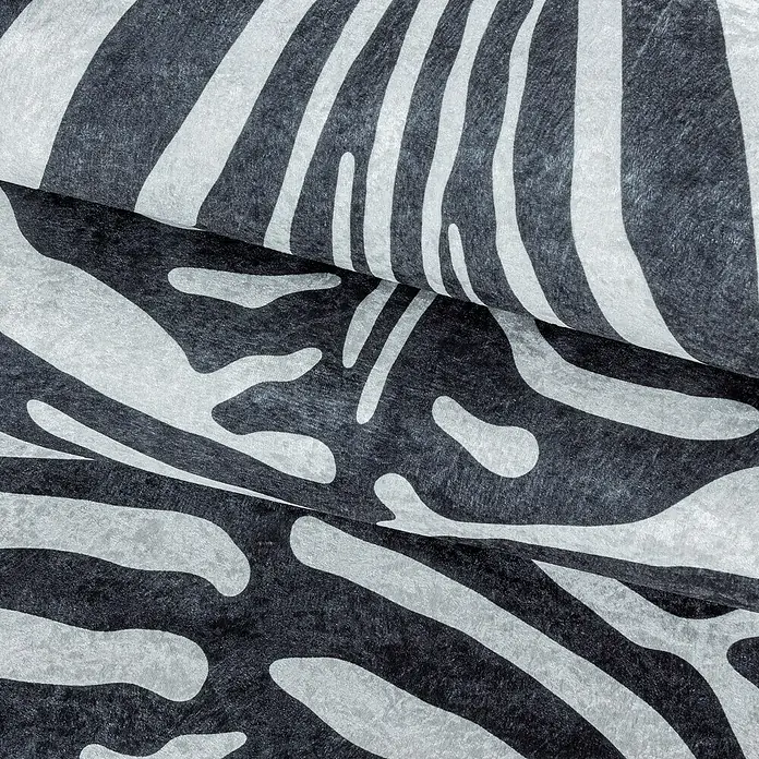 Flachgewebeteppich Etosha - Zebra, Schwarz, 200 x 150 cm, 100 % Polyester - Detailaufnahme von Stoff mit Zebra-Muster in Schwarz und Weiß, gefaltet und strukturiert für eine dynamische Optik.