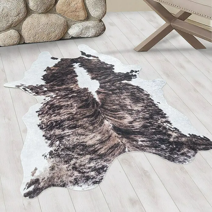 Flachgewebeteppich Etosha - Kuh, Braun/Weiß, 135 x 100 cm, 100 % Polyester - Ein Kuhfellteppich in Braun- und Weißtönen liegt auf einem Holzboden und verleiht dem Raum eine rustikale Note.