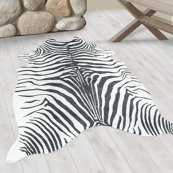 Flachgewebeteppich Etosha - Zebra, Schwarz, 200 x 150 cm, 100 % Polyester - Detailaufnahme eines Zebra-Kuhfellteppichs auf einem Holzboden, der eine stilvolle und wilde Note in den Raum bringt.