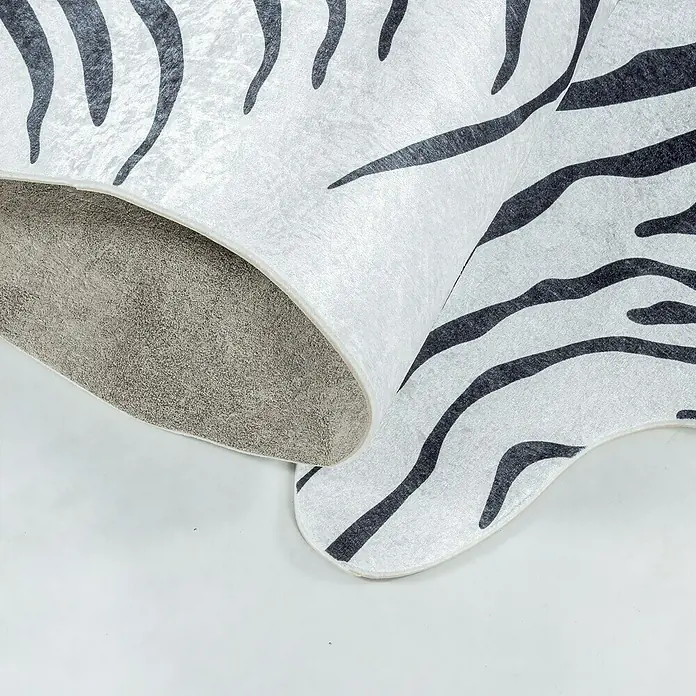 Flachgewebeteppich Etosha - Zebra, Schwarz, 200 x 150 cm, 100 % Polyester - Nahaufnahme eines Tierfells mit Zebramuster, das auf einer hellen Oberfläche liegt. Die Unterseite des Fells ist sichtbar und zeigt eine graue Textur.