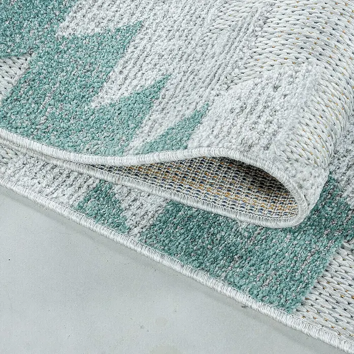 Outdoor-Teppich Bahama II - Blau, 200 x 140 cm, 100 % Polypropylen - Nahaufnahme eines mintgrün-weißen Teppichs mit geometrischem Muster, teilweise aufgerollt, der seine Textur und Unterseite zeigt.