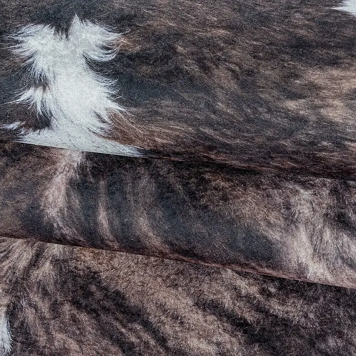 Flachgewebeteppich Etosha - Kuh, Braun/Weiß, 135 x 100 cm, 100 % Polyester - Nahaufnahme eines Kuhfellteppichs mit kontrastierenden Braun- und Weißtönen, der eine warme und natürliche Atmosphäre erzeugt.\n