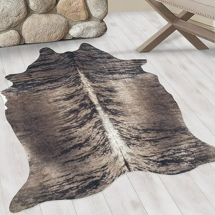 Flachgewebeteppich Etosha - Kuh, Braun/Grau, 200 x 150 cm, 100 % Polyester - Detailaufnahme eines braun-schwarzen Kuhfellteppichs mit weißem Mittelstreifen auf einem hellen Holzboden, der eine gemütliche Atmosphäre schafft.