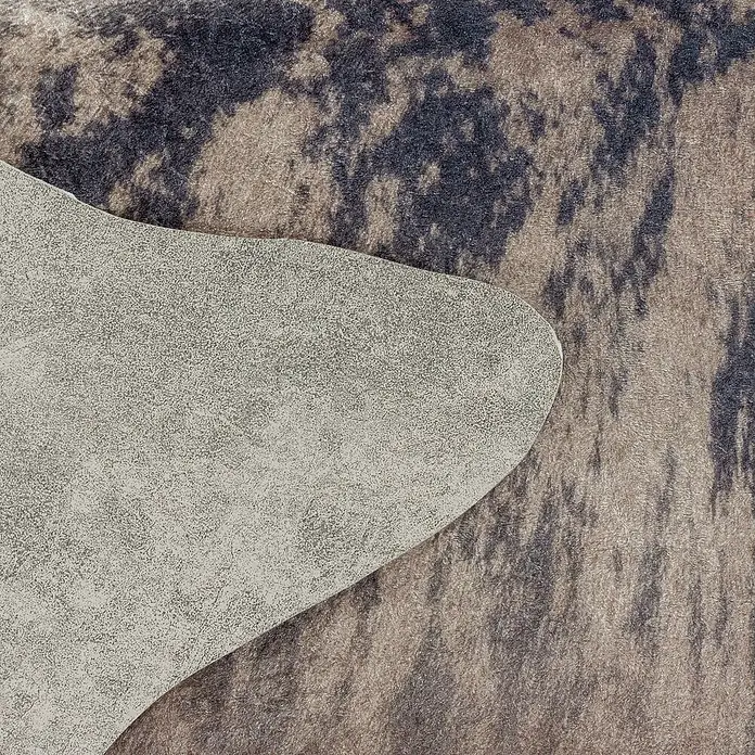 Flachgewebeteppich Etosha - Kuh, Braun/Grau, 200 x 150 cm, 100 % Polyester - Nahaufnahme eines Teppichs mit Kuhfellmuster, teilweise von einem hellgrauen Material bedeckt, das eine interessante Texturkombination zeigt.