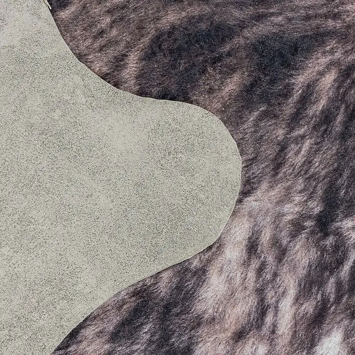 Flachgewebeteppich Etosha - Kuh, Braun/Weiß, 135 x 100 cm, 100 % Polyester - Detailansicht eines Lederstücks auf einem gemusterten Teppich, das die Texturen beider Materialien hervorhebt.