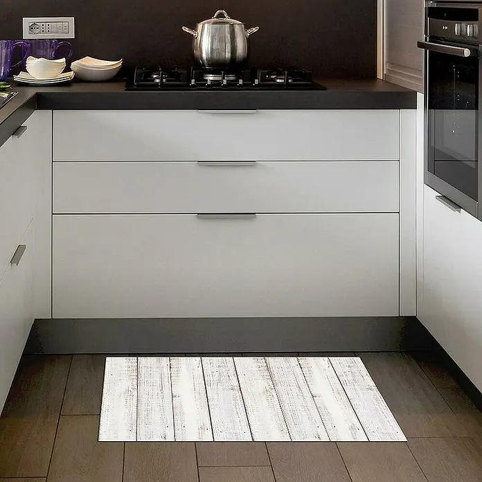 Alfombra de vinilo Croma Madera - Blanco, 75 x 45 cm, PVC - Una alfombra de cocina rectangular con un diseño de madera blanca se encuentra en un piso de madera oscura frente a gabinetes de cocina blancos.