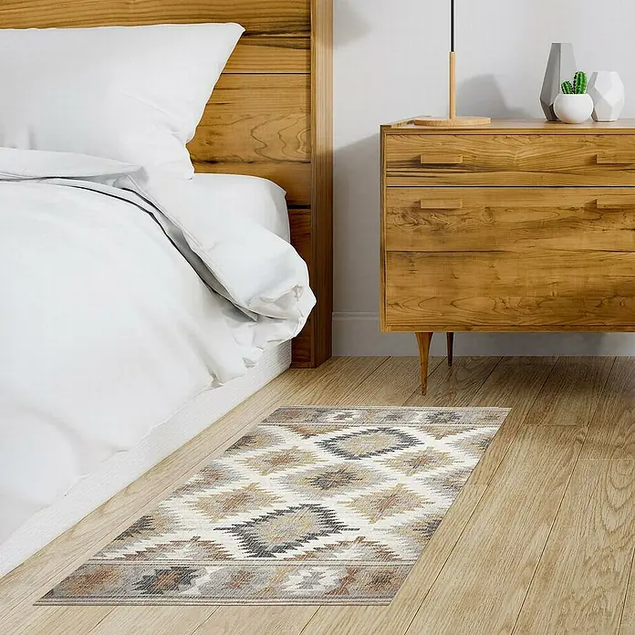 Alfombra de vinilo Croma Rombos - Gris, 110 x 50 cm, PVC - Una alfombra con motivos geométricos se encuentra frente a una cama y una cómoda de madera. La alfombra presenta colores neutros y un diseño llamativo.