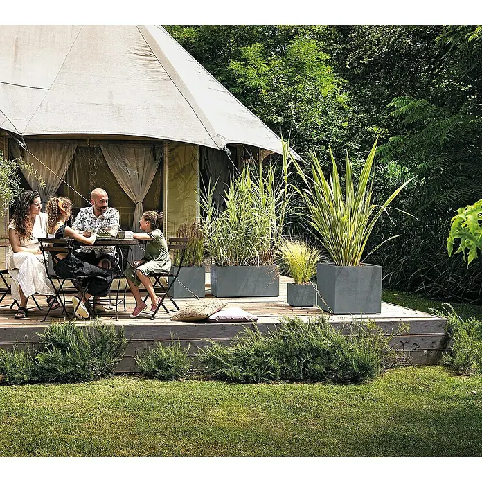 Deroma Millennium Pflanzkasten - Außenmaß (L x B x H): 79 x 39 x 39 cm, Kunststoff, Ashgrey, Mit Bewässerungssystem - Eine Familie sitzt um einen Tisch auf einer Terrasse mit grau Pflanzgefäßen, die mit verschiedenen Pflanzen gefüllt sind.