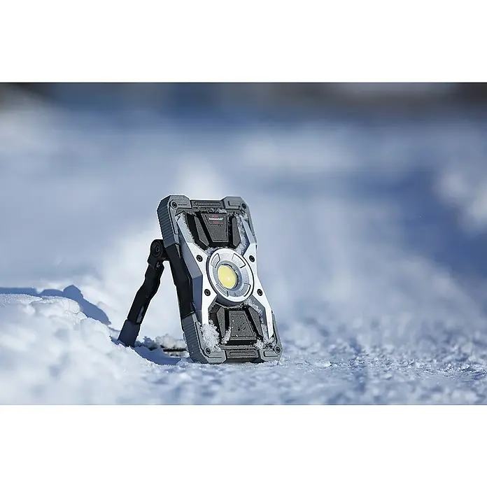 Brennenstuhl Mobiler LED-Strahler Rufus - Akkubetrieben, 30 W, L x B x H: 5 x 14 x 21 cm, IP65 - Nahaufnahme einer tragbaren Arbeitsleuchte von brennenstuhl® im Schnee, die Robustheit und Funktionalität vereint.