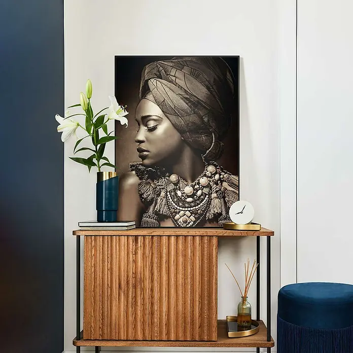 Reinders Bild Slim Frame Black - African Beauty, B x H: 50 x 70 cm - Das Foto zeigt eine stilvolle Kommode aus Holz mit einem dekorativen Schwarz-Weiß-Porträt und weißen Lilien in einer Vase.
